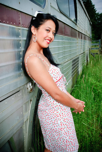 Attractive petite woman leaning against bus in field