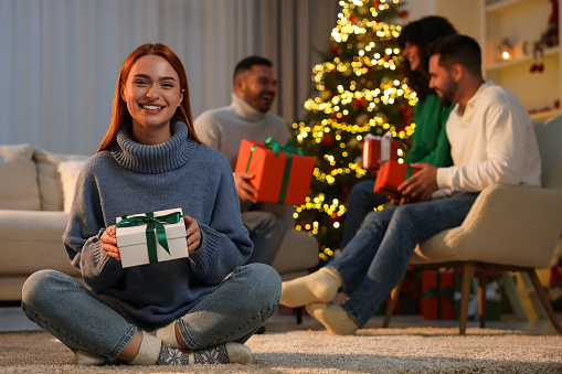 Christmas celebration in circle of friends. Happy young woman with gift box at home, selective focus