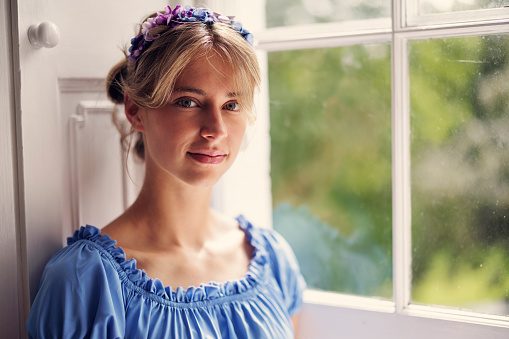 Portrait of young woman wearing a regency era dress near a window.\nShot with Canon R5