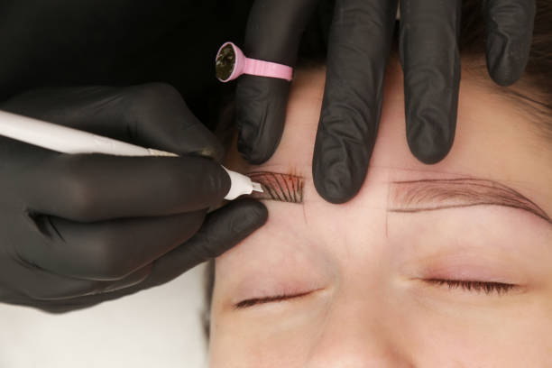 istock Microblading - semi-permanent tattooing technique used for the eyebrows by creating an illusion of a more defined and fuller brow. Artist makes tiny hair-like strokes to create a natural looking brows 1828964207
