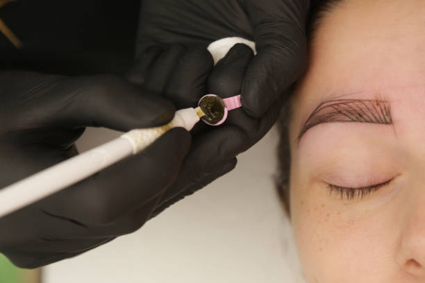 istock Microblading - semi-permanent tattooing technique used for the eyebrows by creating an illusion of a more defined and fuller brow. Artist makes tiny hair-like strokes to create a natural looking brows 1828964209