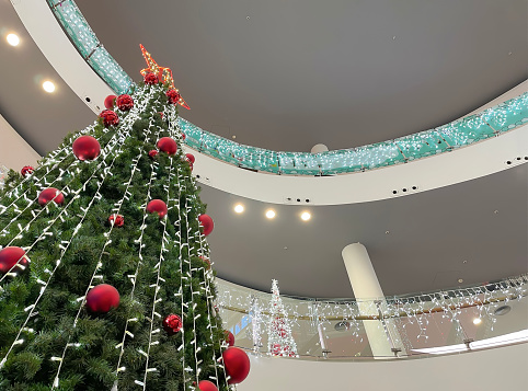 a big christmas tree inside a shopping mall seen from below in perspective, decorated with red balls and a big star at the top, christmas shopping, horizontal