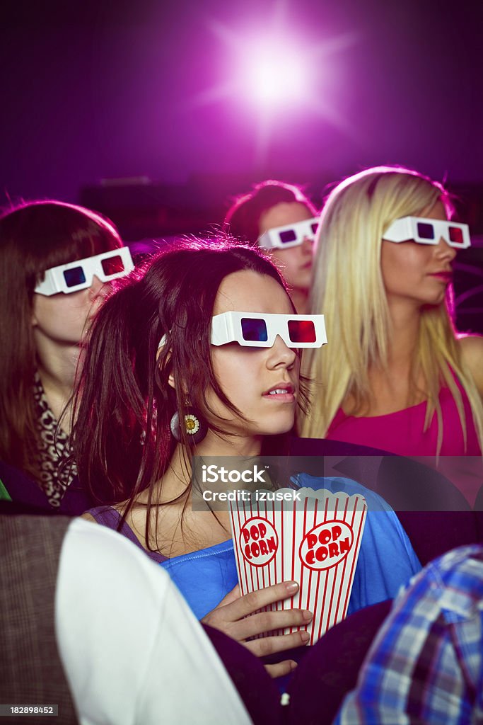 Young people in 3D move theater "Group of young adult people wearing 3D glasses, sitting in the cinema  and watching 3D move. Teenage girl sitting in the middle holding box of popcorn in hand." 3-D Glasses Stock Photo