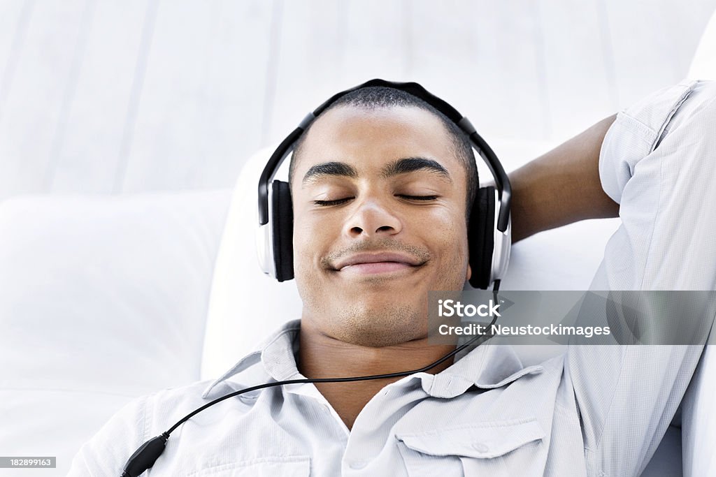 Young Man Listening to Headphones Handsome young man reclines back with his eyes closed while listening to music on his headphones.  Horizontal shot. Headphones Stock Photo