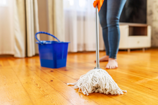 Young woman in protective gloves washing a wooden floor with a mop, doing homework, routine cleaning, cleaning job concept