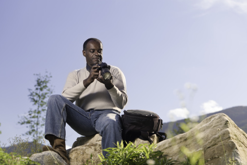 Mature adult african american man with dslr camera gear looking at image on back of camera.
