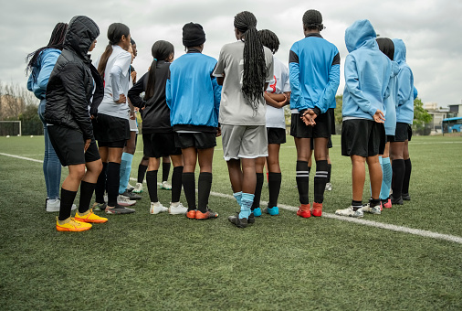 Girls soccer team standing in circle listening to the coach at sports court outdoors during training session
