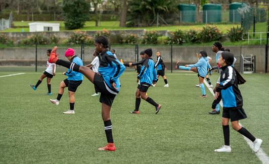 Young female soccer players in sports clothing doing stretching workout during training session on soccer field