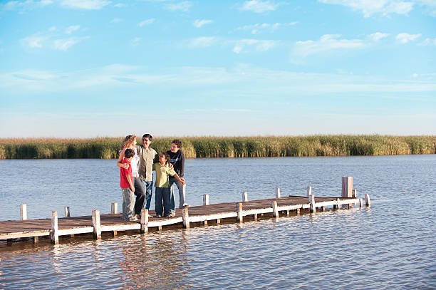 Young family bonding by pond, parents pointing out ducks to their baby, enjoying nature in a sunny park