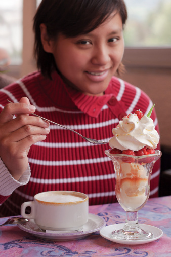 A yummy ice cream sundae with strawberries and whip cream.  Focus is on sundae.