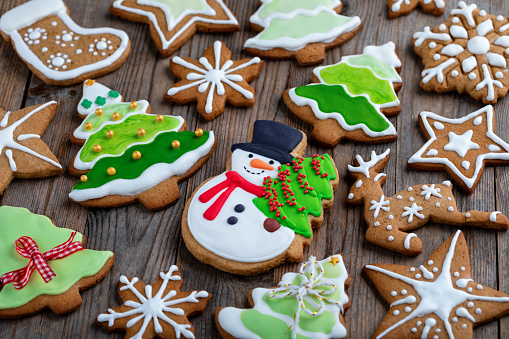 Festive delicious homemade Christmas cookies decorated with icing on wooden table. Gingerbread cookie in the shape of snowman with fir tree, Christmas tree, deer, snowflake and stars.