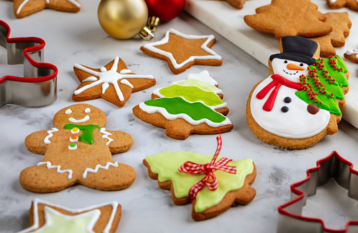 Delicious homemade Christmas cookies decorated with icing on white background. Gingerbread cookie in the shape of snowman with fir tree, Christmas trees, stars shape and gingerbread man. Concept of preparing Christmas cookies for the winter holidays.