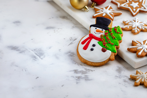 Gingerbread cookie in the shape of snowman with Christmas tree and  gingerbread cookies in the shape of stars and snowflakes decorated with icing on white background with copy space.