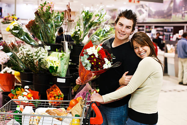 웃는 젊은 커플입니다 안기 그가 buys 꽃을 슈퍼마켓 - florist supermarket flower bouquet 뉴스 사진 이미지