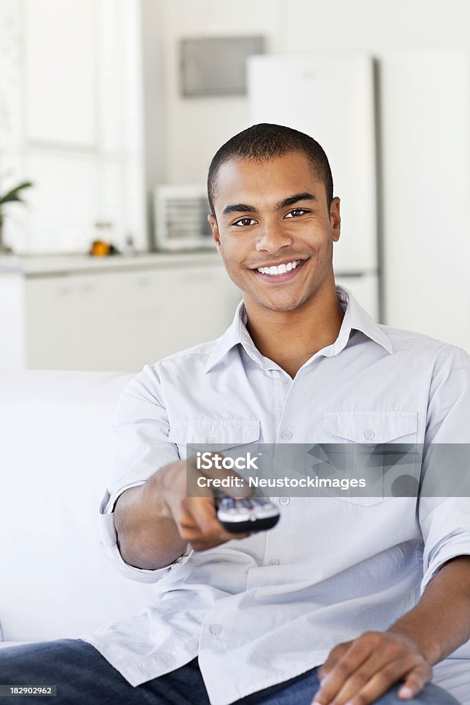 Young Man Watching Television Handsome young man uses a remote control to change channels while sitting on the couch. He is smiling into the camera. Vertical shot. 20-29 Years Stock Photo