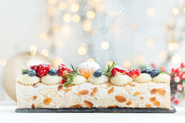 istock Meringue roll sprinkled with powdered sugar decorated with blueberries, pomegranate and almond flakes on the white background with blurred bokeh lights. Christmas festive pastry 1829047032