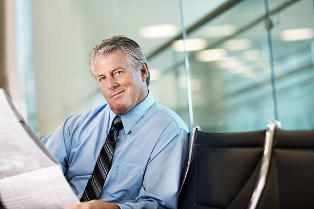 Mature businessman reading a newspaper at airport Portrait of a confident mature businessman reading a newspaper at airport newspaper airport reading business person stock pictures, royalty-free photos & images