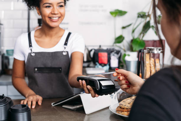 istock Smiling barista in apron holding POS terminal while customer paying by card 1829080095