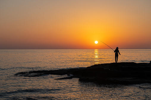 Silhouette of a girl fishing with a fishing rod in the sea at sunset.