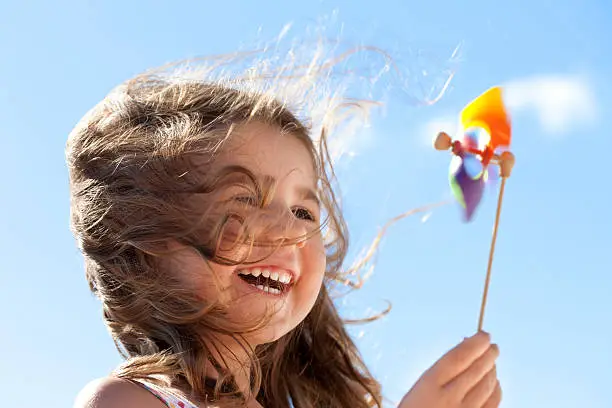 Little happy girl laughing and holding a pinwheel in front of a bright sky. The wind is blowing her hair illuminated by the sunlight. Conceptual image about environment and happiness.Similar pictures: