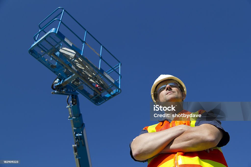 Lift Operator A construction worker stands beneath his equipment. Scissor Lift Stock Photo
