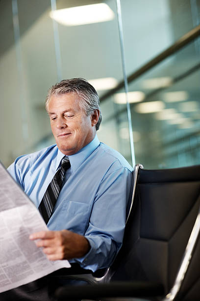 Mature businessman reading a newspaper at airport Confident mature businessman reading a newspaper at airport newspaper airport reading business person stock pictures, royalty-free photos & images