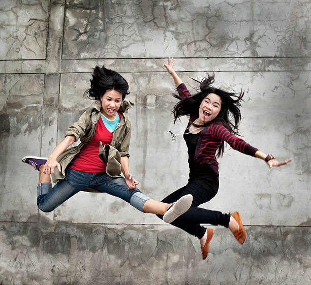 Two beautiful girls are enjoying their day. They are outdoor, smiling and jumping.