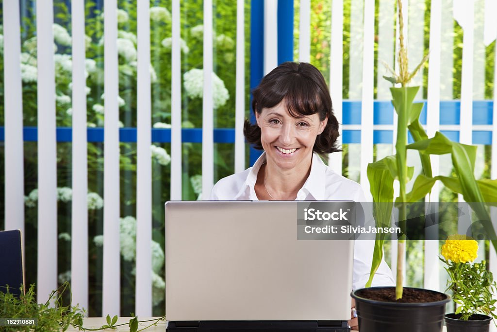 Donna d'affari circondata da piante - Foto stock royalty-free di 50-54 anni