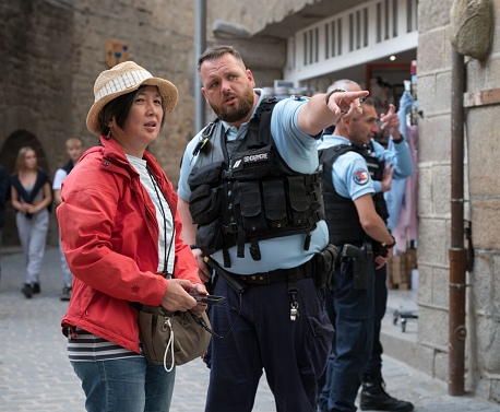 Pontorson, France – October 13, 2023: A French police officer giving an address to an Asian tourist on Mont Saint Michel