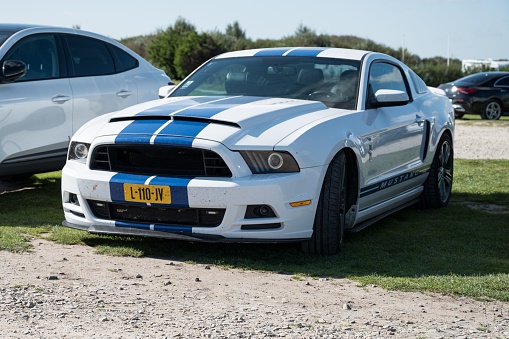 Normandy, France – October 13, 2023: An out of focus photo of a typical fifth generation Ford Mustang American sports car, white with Shelby blue stripes