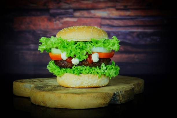 istock Hamburger with onion, tomato and lettuce on black surface, old wooden background 1829117415