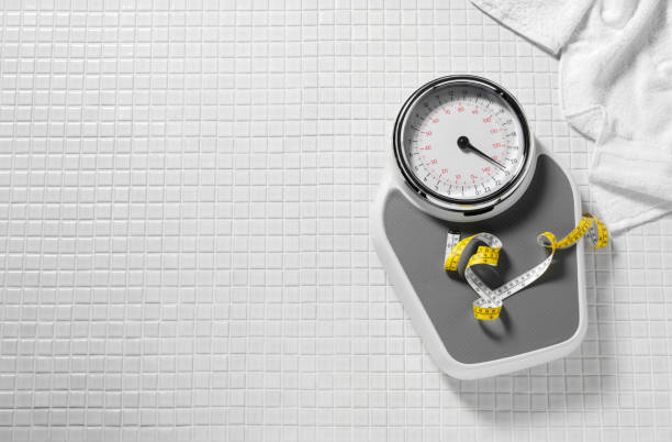 Bathroom Scales and Tape Measure Tape measure on bathroom scales on a white tiled background with a bath robe and copy space.Click on the link to see more of my nutrition and medical images Weights stock pictures, royalty-free photos & images