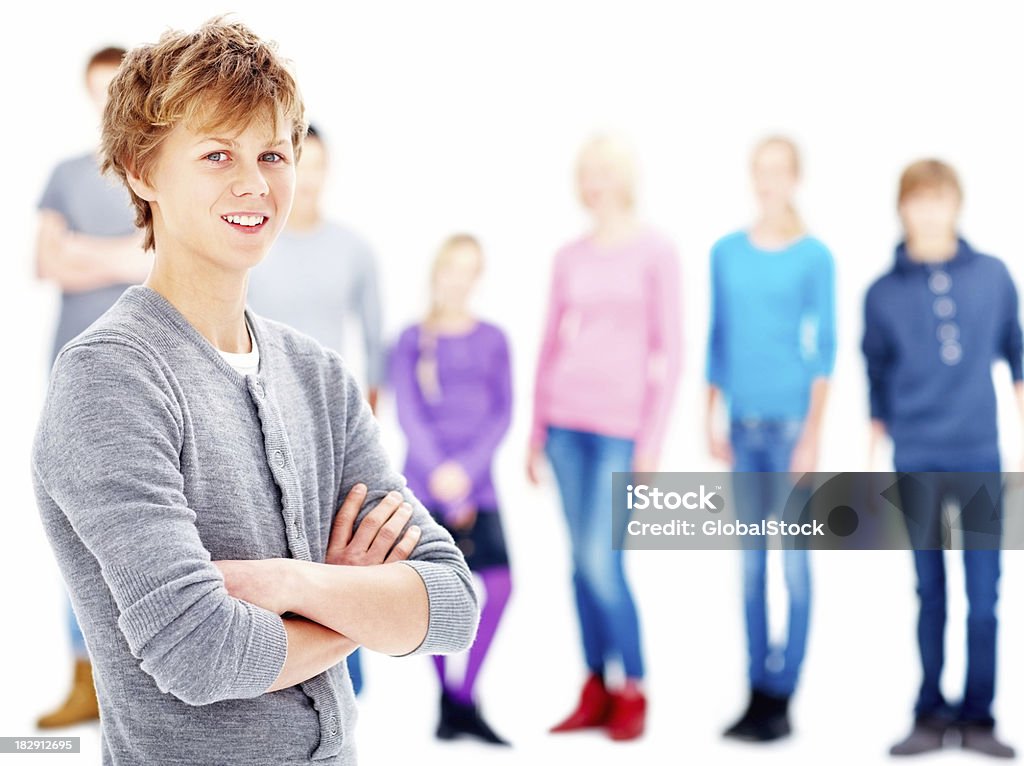 Smiling teenage boy with friends in the background Portrait of a happy teenage boy standing with arms crossed and friends in the background against white Close-up Stock Photo