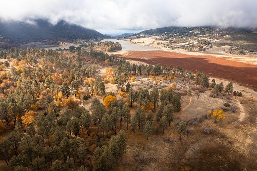 Elevated above Julian and the Stonewall Mine Trail, this breathtaking aerial view unveils a picturesque scene in Cuyamaca Rancho State Park, San Diego County, California. Evergreen and autumnal trees frame a tranquil clearing, with mountains, lake, distant houses, and the sky completing the harmonious panorama