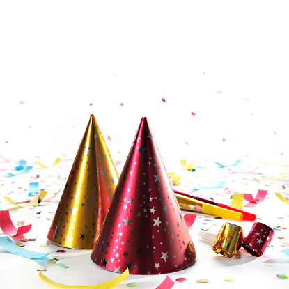 Party decorations: hats, whistles, horns, confetti isolated on white background. Square composition, copy space, studio shot.