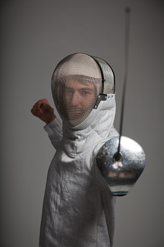 A fencer points his foil at the camera.