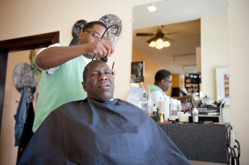 Candid shot in ambient light of a black barber shaving head of African American client.