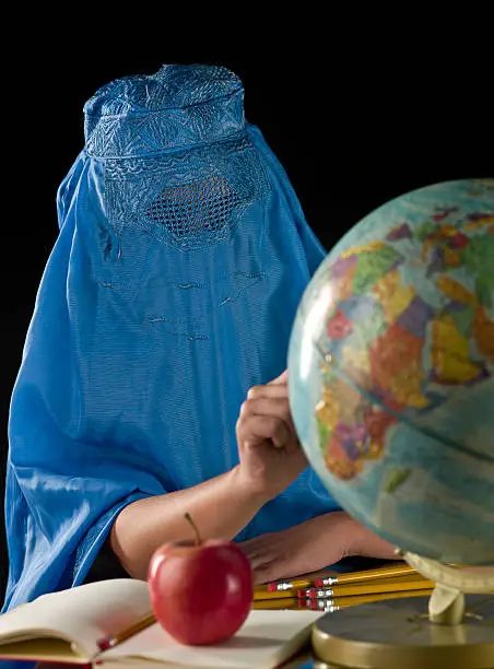 Little Afghan Girl at the School pointing at a desktop globe map on black background (this picture has been taken with a Hasselblad H3D II 31 megapixels camera)