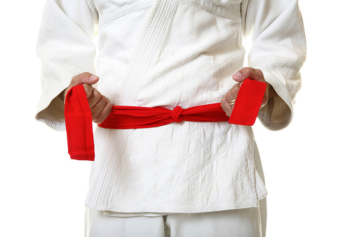 Young sporty karate man in kimono holding belt in hands