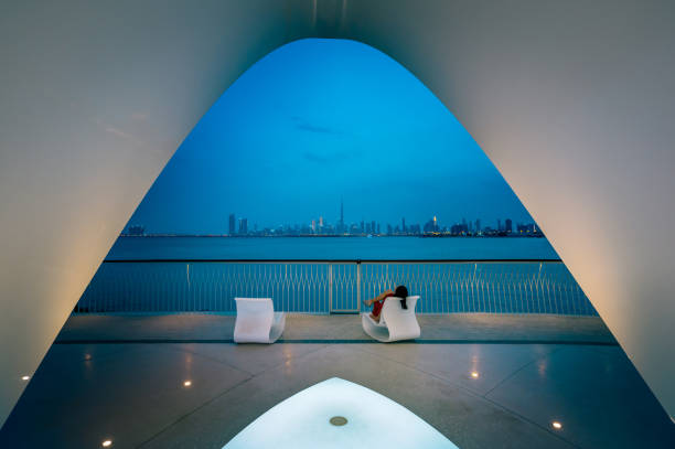 Woman standing enchanted, gazing at the breathtaking Dubai skyline from Creek Harbour. The city comes alive with twinkling lights against the dusky sky, creating a scene of tranquil beauty and urban allure
