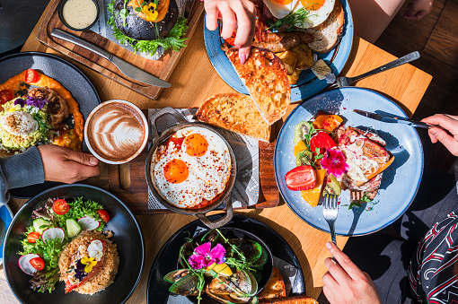 Table top view of breakfast food displayed on table, people eating food.