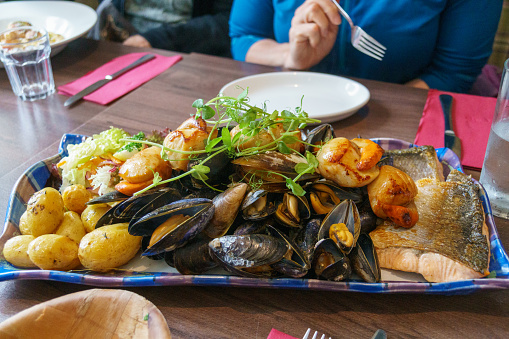 Huge seafood platter with fish, mussels, scallops. An eager diner holds a fork in the background.