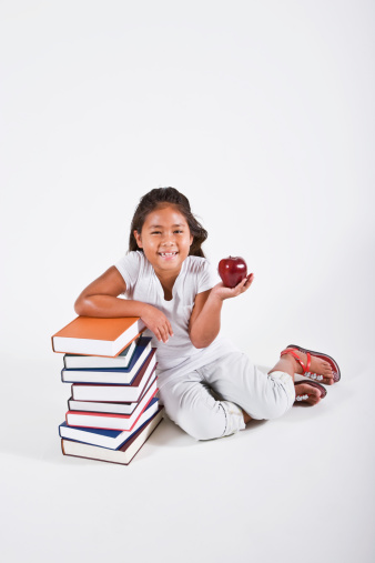 Multi-ethnic child eager to learn, sitting beside stack of books (girl, 7 years)