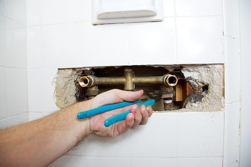 Plumber's hand loosens a nut to fix a leak in a shower