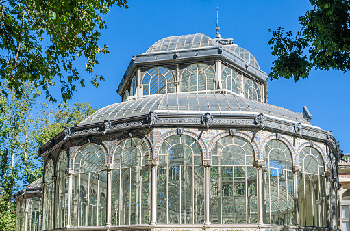 Madrid, Spain - August 18, 2019: Palacio de Cristal (Glass Palace), a metal and glass structure located in the Retiro Park in Madrid, Spain, built in 1887 for the Philippines Exposition. Currently it belongs to the Reina Sofia Museum