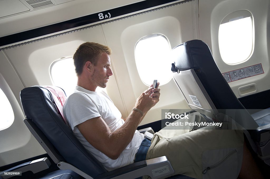 Viaggiare uomo seduto un SMS al cellulare con Sedile di aeroplano - Foto stock royalty-free di Abbigliamento casual