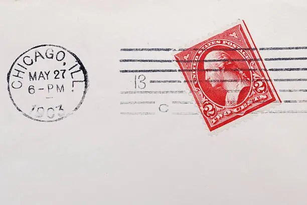 "Vintage, canceled, red,  two cent George Washington postage stamp on weathered envelope paper from 1903. Postmark Chicago, May 27, 1903. Stamp is angled on envelope."