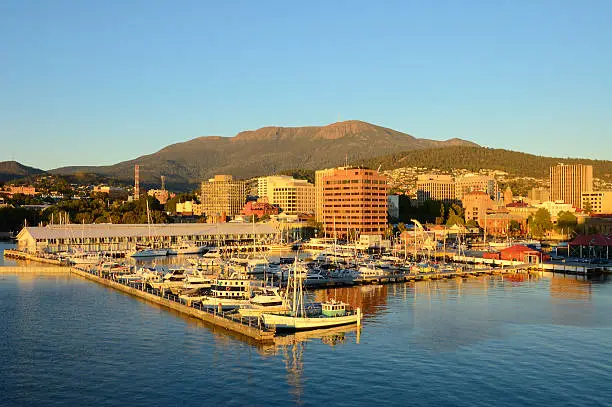 A view of Sullivans Harbor in Hobart, Tasmania on a clear day with Mt. Wellington rising in the background. The Broadcast Australia Tower, or NTA, sticks up on Mt. Wellington like a rocket poised for takeoff,