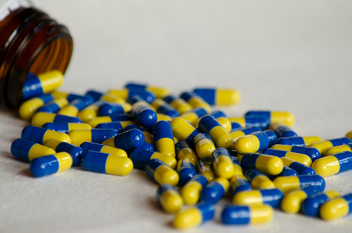 remedies in capsules on a white background with blue and yellow pills coming out of the pharmaceutical bottle