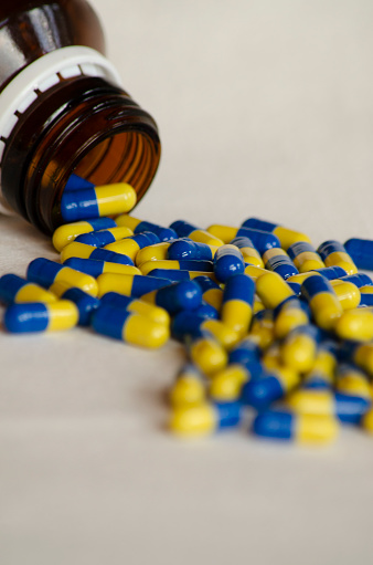 remedies in capsules on a white background with blue and yellow pills coming out of the pharmaceutical bottle